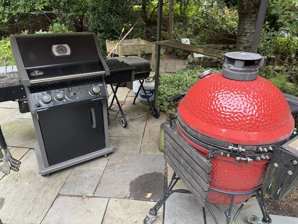 A gas grill and a red kamado smoker on the stone patio
