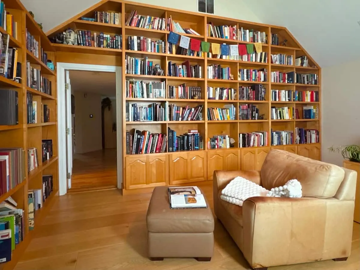A wall of bookshelves rising to a peaked ceiling, with a leather sofa and ottoman